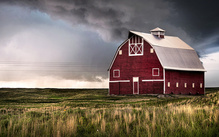 Red barn sitting in a field with grey and stormy skies
